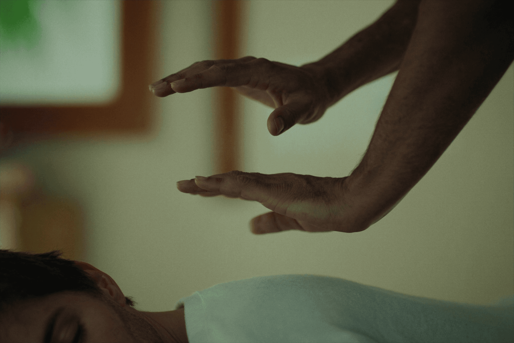 Practitioner's hands resting gently and still above a relaxed clothed person during a soothing reiki session