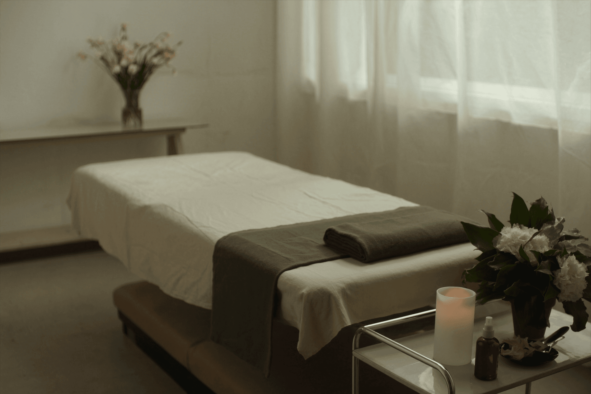 Serene treatment room with a linen-dressed couch, candle and plant, prepared for a calming relaxation therapy session