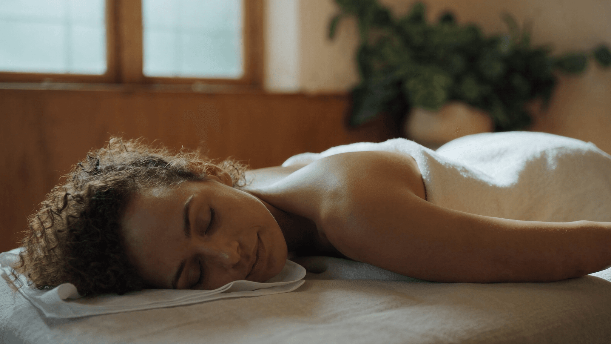 Relaxed woman lying face-down under a towel on a massage table, showing what to expect at a first massage