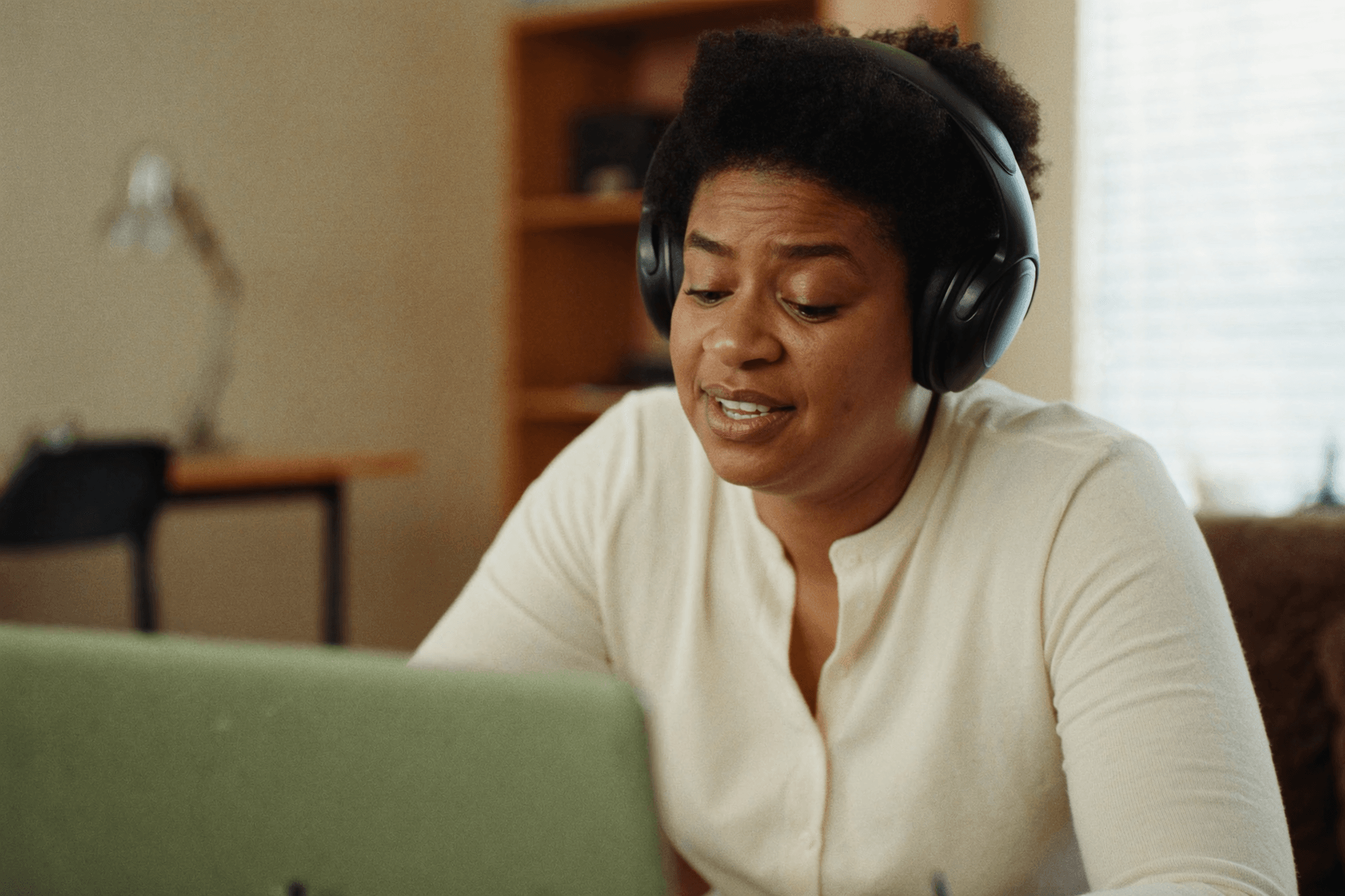 Person wearing headphones during a remote hypnotherapy video call in a calm, sunlit home study