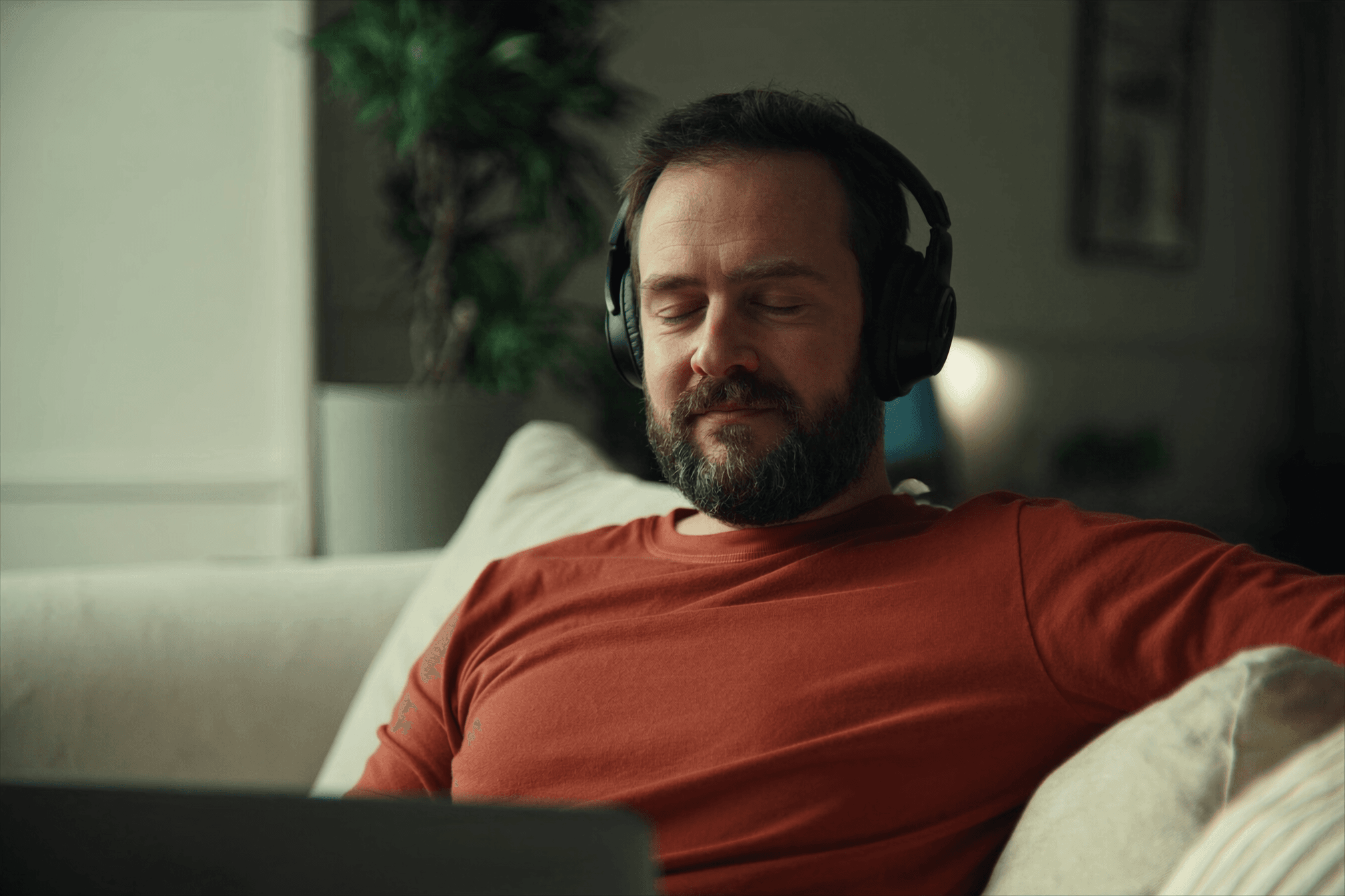 Man relaxing at home with headphones and laptop during an online hypnotherapy session in the UK.